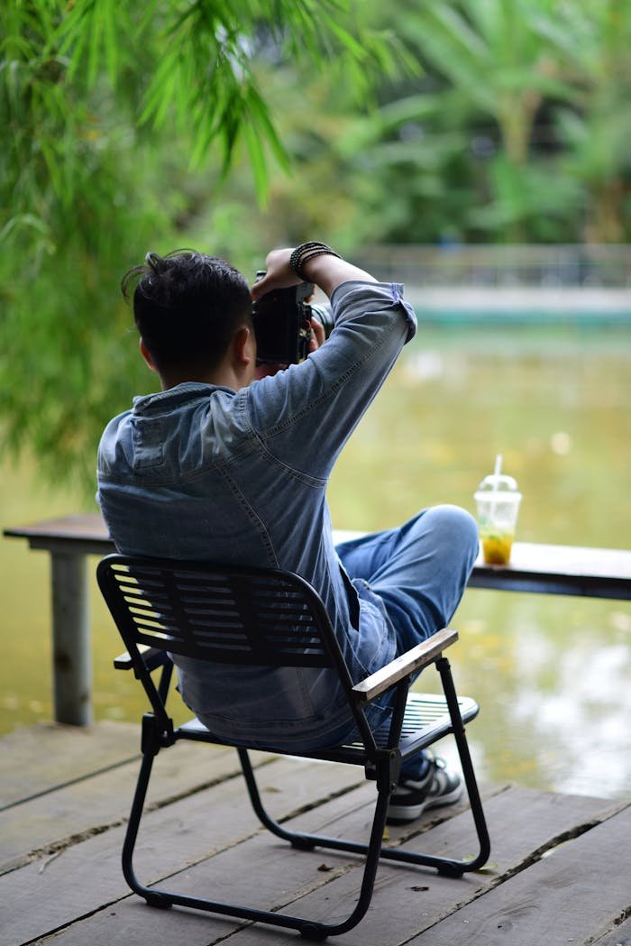 A photographer sits by a pond, enjoying a peaceful moment outdoors with a camera in hand.